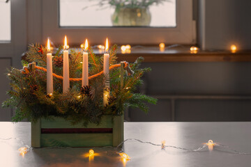 advent decoration with fir branches and four burning candles in wooden basket on white table at home