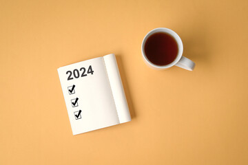 2024 checklist on notepad with cup of coffee. Top view. On yellow background.