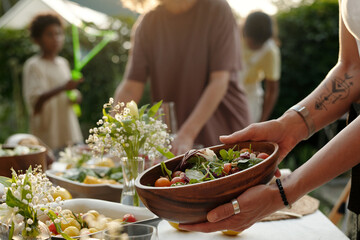 Focus on hands of young woman putting wooden bowl with fresh homemade vegetable salad on table...