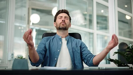 Handsome relaxed young handsome businessman male worker sitting at workplace with folded in mudra gesture hands, reducing stress during workday, meditating or doing yoga breathing exercises in office.