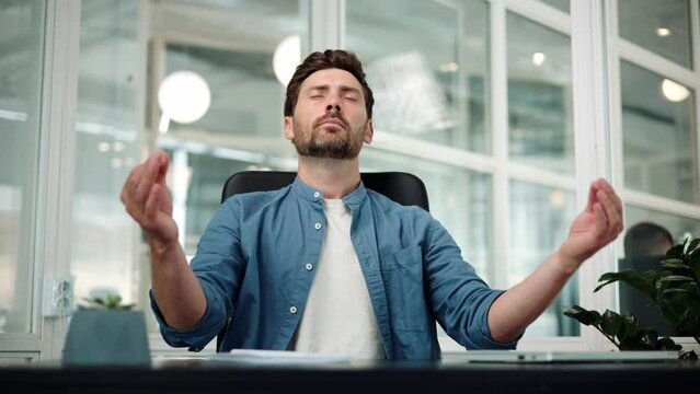 Handsome relaxed young handsome businessman male worker sitting at workplace with folded in mudra gesture hands, reducing stress during workday, meditating or doing yoga breathing exercises in office.