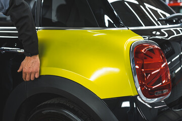 unknown man touching a neon yellow vinyl wrap added on a black car, repair shop. High quality photo