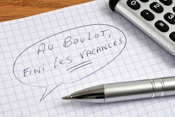 Au boulot, fini les vacances écrit sur une feuille de papier quadrillée avec un stylo