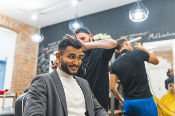 Skilled barber styling his Indian client hair using hair clipper in a barbershop. High quality photo