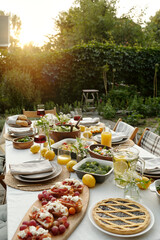 Part of long table served with various food and snacks prepared for outdoor family dinner standing in front of camera in the garden