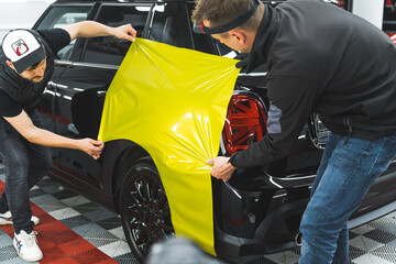 skilled professionals using special lime vinyl film to wrap a black car. Vehicle wrapping...