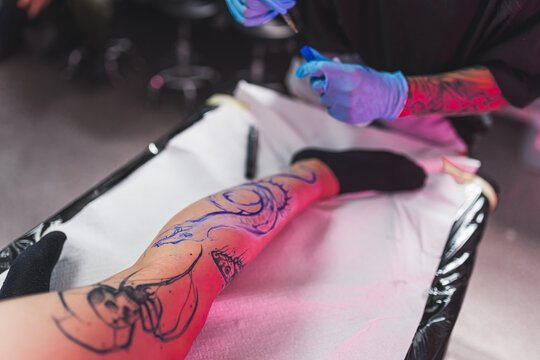 High angle perspective of an artist performing freehand technique - drawing directly onto the client's skin. Leg tattoo concept. High quality photo