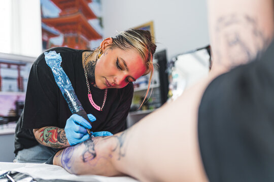Leg tattoo process. Female client lying on tattooing bed and observing her female tattooing artist drawing a design on her calf. High quality photo
