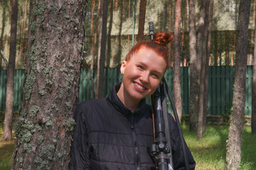 Fototapeta na wymiar Young redhead woman protecting her house or on tactical gun training classes. Woman with weapon. Outdoor Shooting Range. Lady with rifle machine gun in the forest