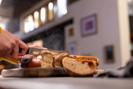 Hands of indian man in apron cutting bread in kitchen, copy space