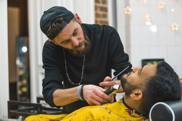 Barber trimming beard of a client using handheld trimmer in a modern barbershop. High quality photo