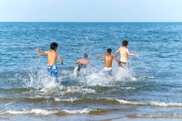 Four boys run into the sea with splashes