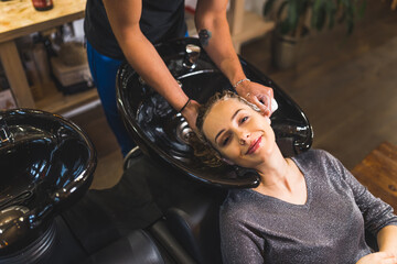 Plakat Smiling client having her hair shampooed by hairdresser at sink in a barber shop. Top view. High quality photo