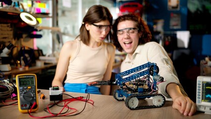 Two young happy engineers fixing a mechanical robot car in the workshop, using VR virtual reality headsets