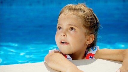 Little girl in sunglasses resting on white pool balloon