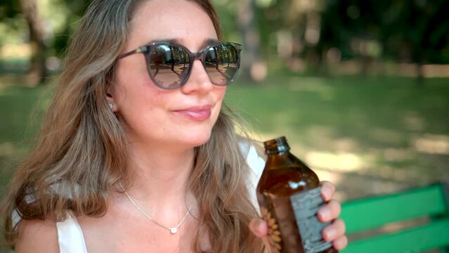 Woman drinking kombucha lemonade in a gree park, slow motion