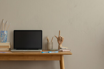 Aesthetic composition of simple office interior with copy space, wooden desk, computer, books, sculpture, glass cup with pencils, brown wall and personal accessories. Home decor. Template.