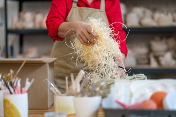 Female owner of small pottery shop standing by table and packing ordered item for clients.