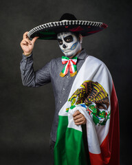 Portrait of catrin wearing charro hat and showing mexican flag. Day of the dead.