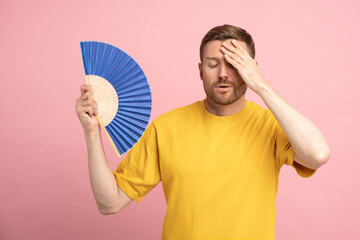 Too hot. Sweaty tired middle aged man touching forehead using paper fan suffer from heat, feels...