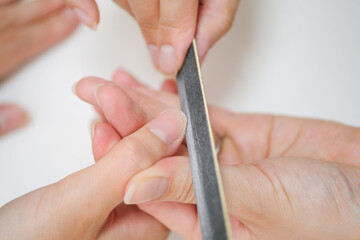 ネイリストにネイルファイルで爪を整えてもらっている女性の指先のクローズアップ