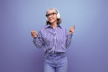 Fototapeta premium Energetic retired woman with gray hair masters headphone technique on a bright studio background