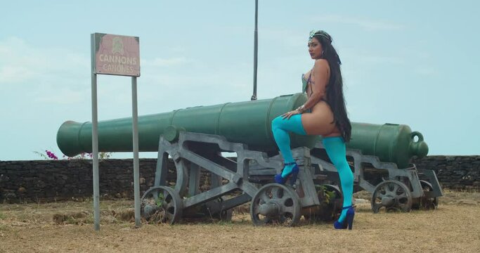 A young girl stands confidently in her eye-catching carnival costume and high heels, striking a pose beside the historic cannons at the fort In a vibrant Caribbean setting