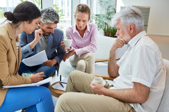 Dedicated business colleagues discussing over documents while sitting together in office lounge