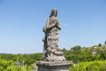 Obraz premium Ancient stone tombstone in form of praying Jesus on cemetery