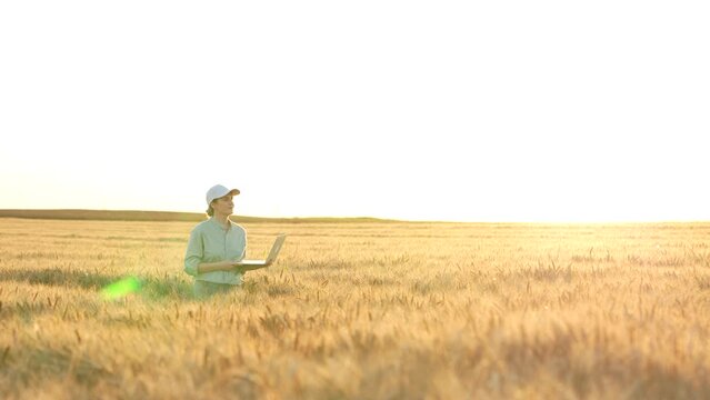 Female farmer with laptop walking through wheat field at sunset