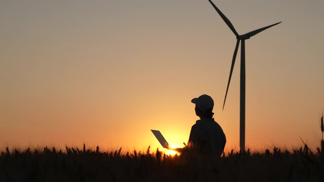 Silhouette of farmer with laptop outside, wind turbines on the horizon