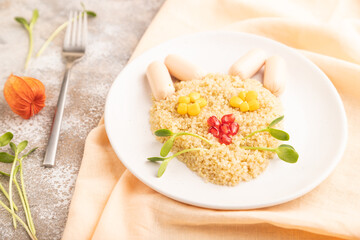 Funny quinoa porridge, and small sausages in form of cat face on brown concrete. side view, selective focus.