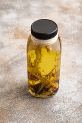 Sunflower oil in a glass jar with various herbs and spices on a brown concrete. Side view.
