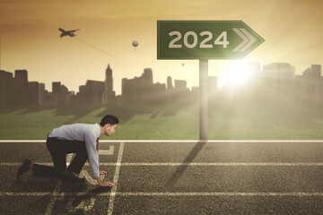 young businessman in ready position to run on the track with 2024 new year numbers