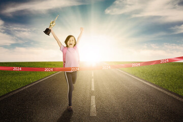 Happy school girl is carrying a trophy while crossing the success line with number 2024