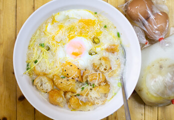 Hot congee or Rice porridge with soft boiled egg served in a white bowl with deep-fried dough stick (crispy patongo) on woodden backgrounds,left copy space fortext.
