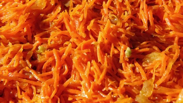 Grated carrots background. Spicy Carrot salad with dressing and spices, onion, garlic. Cooked chopped carrot. Asian dish with condiments, pepper. Food wallpaper spinning. Oriental cuisine. Full Frame