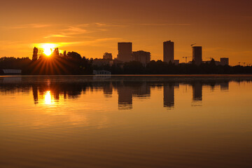 Fototapeta premium Bucharest at sunrise. beautiful morning orange sky landscape of the city skyline and its reflection in Herastrau Lake. Travel to Romania.