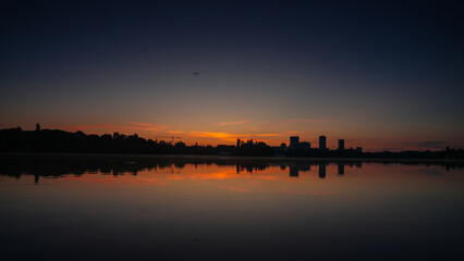 Sunrise over Bucharest. Sunrise photo in the morning dusk with orange and blue sky with the skyline of Bucharest and reflection in Herastrau Lake. Travel to Romania.