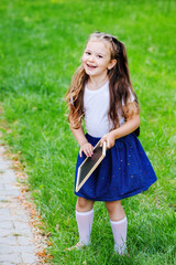Adorable little schoolgirl in park on bright autumn day.