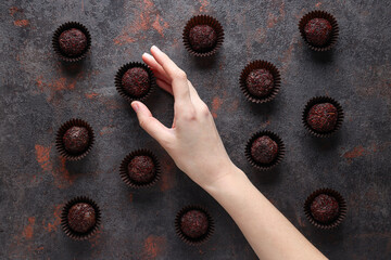 Brigadeiro in paper forms and female hand on dark background, top view
