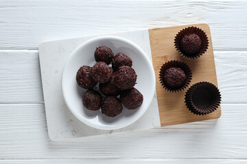Brigadeiro in bowl and on kitchen board on white wooden background, top view