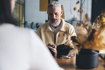 Gray haired male using smartphone at table in workspace