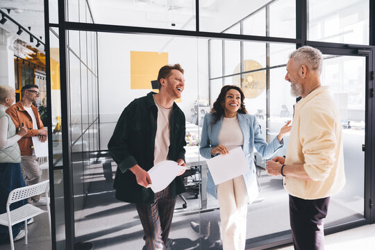 Cheerful diverse colleagues standing with papers in workplace