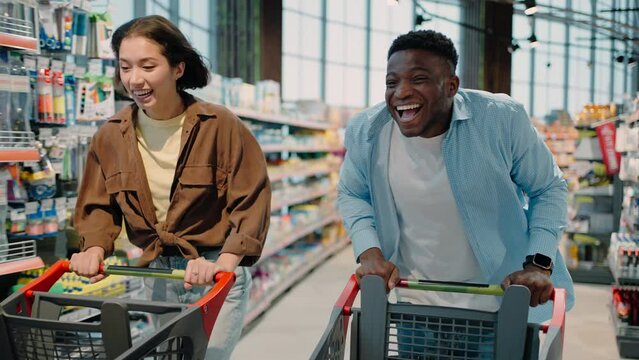 Happy man and woman run with shopping carts in supermarket