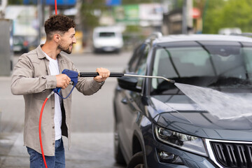 Young handsome man washes a car at a self-service car wash.
