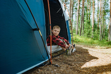 cute caucasian boy wearing hat sitting inside a big touristic tent. Family camping concept