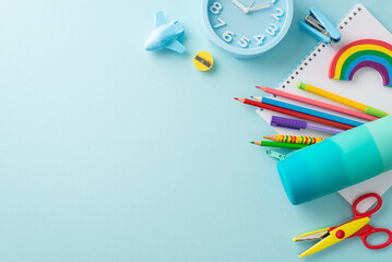 Well-organized drawing station from top view: bright stationery, pencil case, pens, sketchbook, plasticine, stapler, scissors, plane shaped sharpener, clock on soft blue backdrop. Space for text or ad