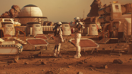 Two astronauts in spacesuits walk toward research station, colony or scientific base on Mars. Solar...
