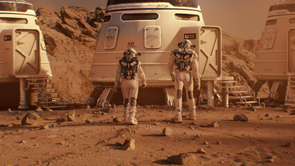 Two astronauts in spacesuits walk toward research station, colony or scientific base on Mars....